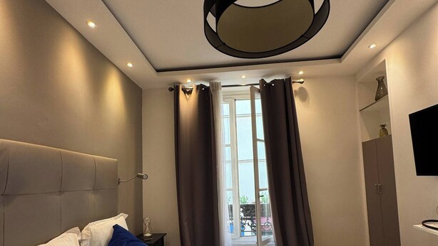 Et moderne hotelværelse med en stor seng, en sengegavl, en loftslampe og udsigt til det fri gennem et vindue med gardiner.