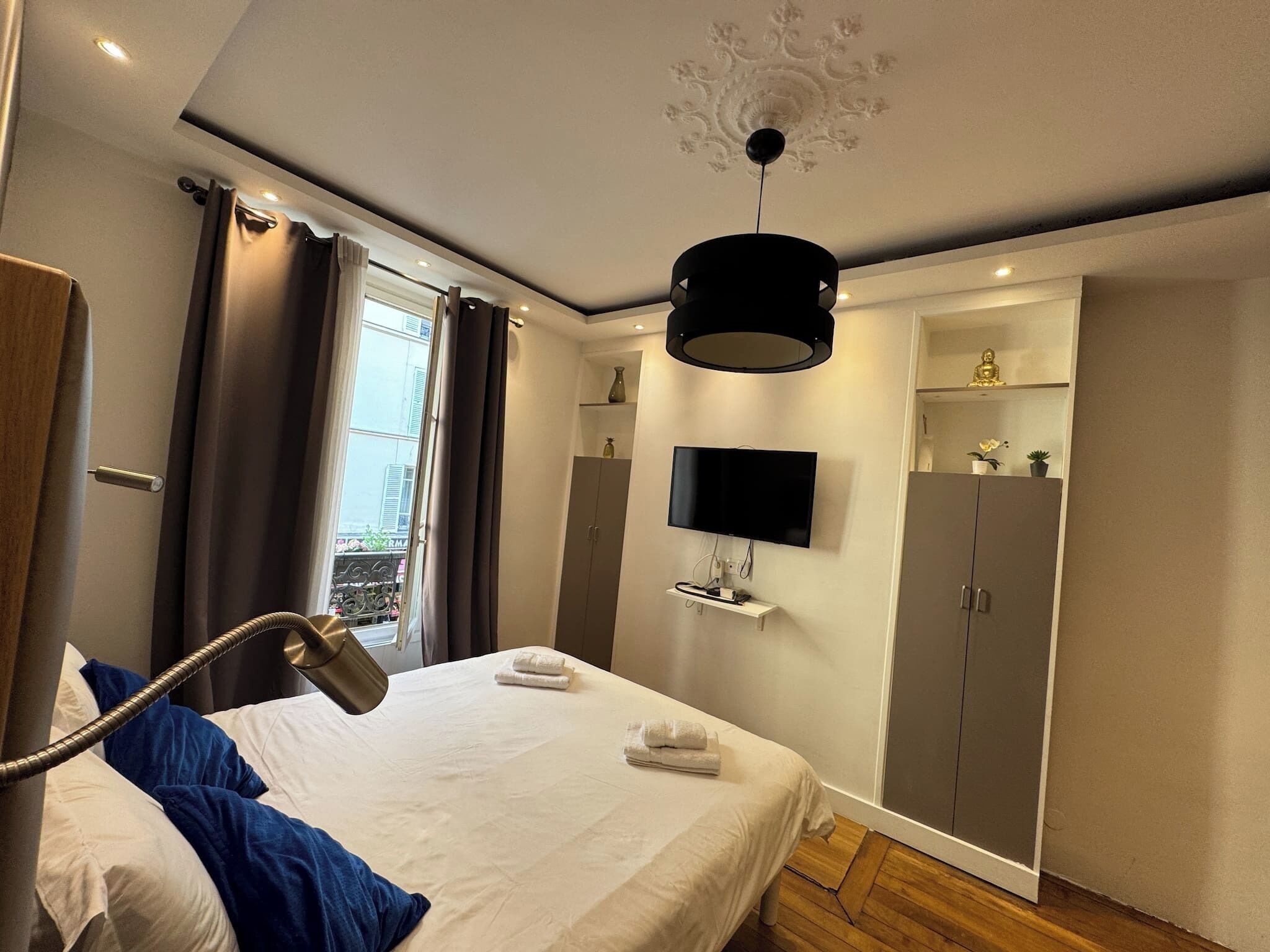 A modern bedroom with a bed, a TV mounted on the wall, a wardrobe, and a ceiling light fixture.