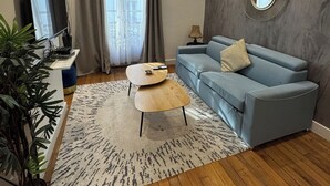 En moderne stue med en blå sofa, et træbord, et fjernsyn og en potteplante.