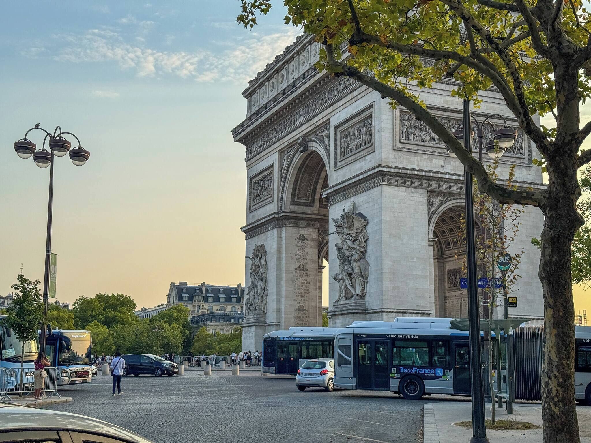 A view of the Arc de Triomphe in Paris, surrounded by trees and street lamps.