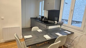 Et moderne køkken med en central ø, et spisebord med stole, og store vinduer med havudsigt.