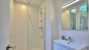 Un baño moderno con ducha de vidrio, un lavabo blanco y un espejo sobre el lavabo.