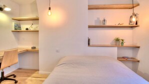 Un dormitorio con cama, escritorio y estanterías con libros y objetos decorativos.