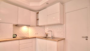 Una cocina compacta con armarios blancos, encimera de madera, pileta de acero inoxidable y salpicadero de azulejos.