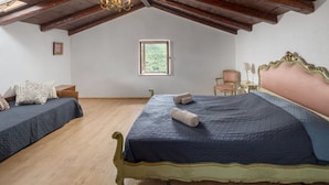 Een slaapkamer met een groot bed, een kleiner bed, een raam, een stoel en een klein tafeltje.