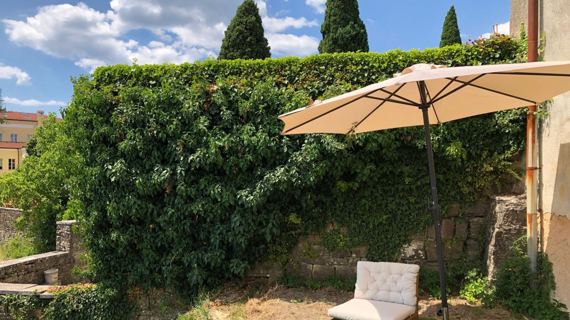 A garden with a chair and an umbrella, surrounded by lush greenery and stone walls.