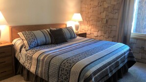 Una cama bien hecha con una colcha estampada, dos lámparas de noche y un cabecero de madera.