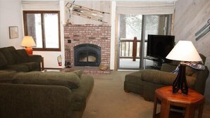 Una sala de estar con chimenea, dos sofás, un televisor y una lámpara.