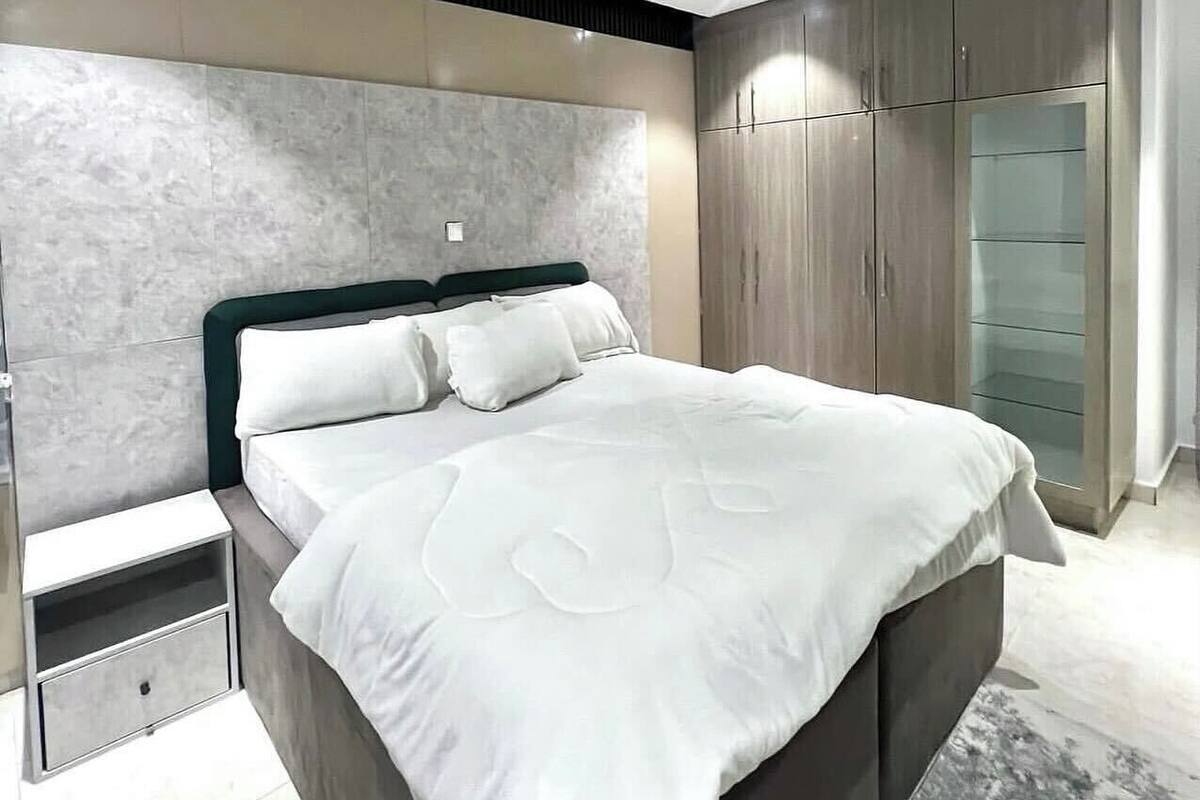 A modern bedroom with a large bed, built-in wardrobe, and a marble headboard.