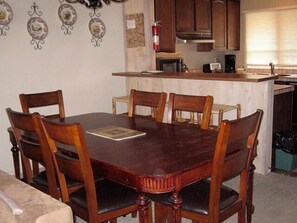 A dining area with a wooden table and chairs, a kitchen in the background, and a fire extinguisher on the wall. - Mammoth Creek Unit 08 (Mammoth Lakes)