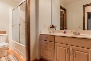 A bathroom with a shower, toilet, vanity with a mirror, and wooden cabinets. - Mammoth Creek Unit 28 (Mammoth Lakes)