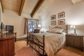 A bedroom with a bed, bedside tables, a window with curtains, a television on a wooden stand, and framed pictures on the wall. - Mammoth Creek Unit 28 (Mammoth Lakes)