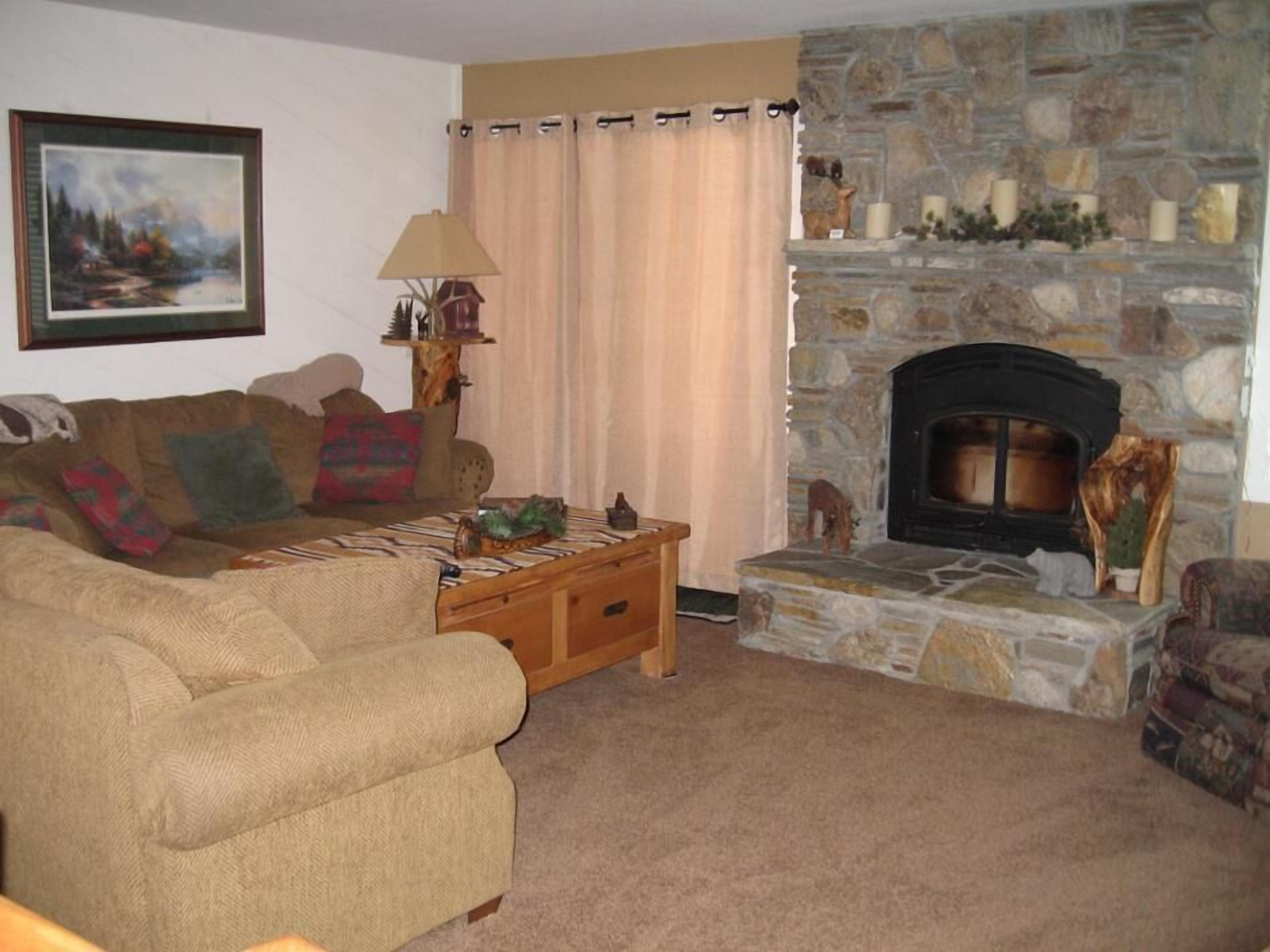 A cozy living room with a stone fireplace, a sofa, a coffee table, and a lamp.