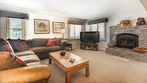 A cozy living room with a stone fireplace, a leather sofa, a wooden coffee table, and a flat-screen TV. - Mammoth Creek Unit 45 (Mammoth Lakes)
