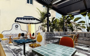 An outdoor seating area with tables and chairs, a patterned wall, and potted plants. - The Standard Lisbon (Lisbon)