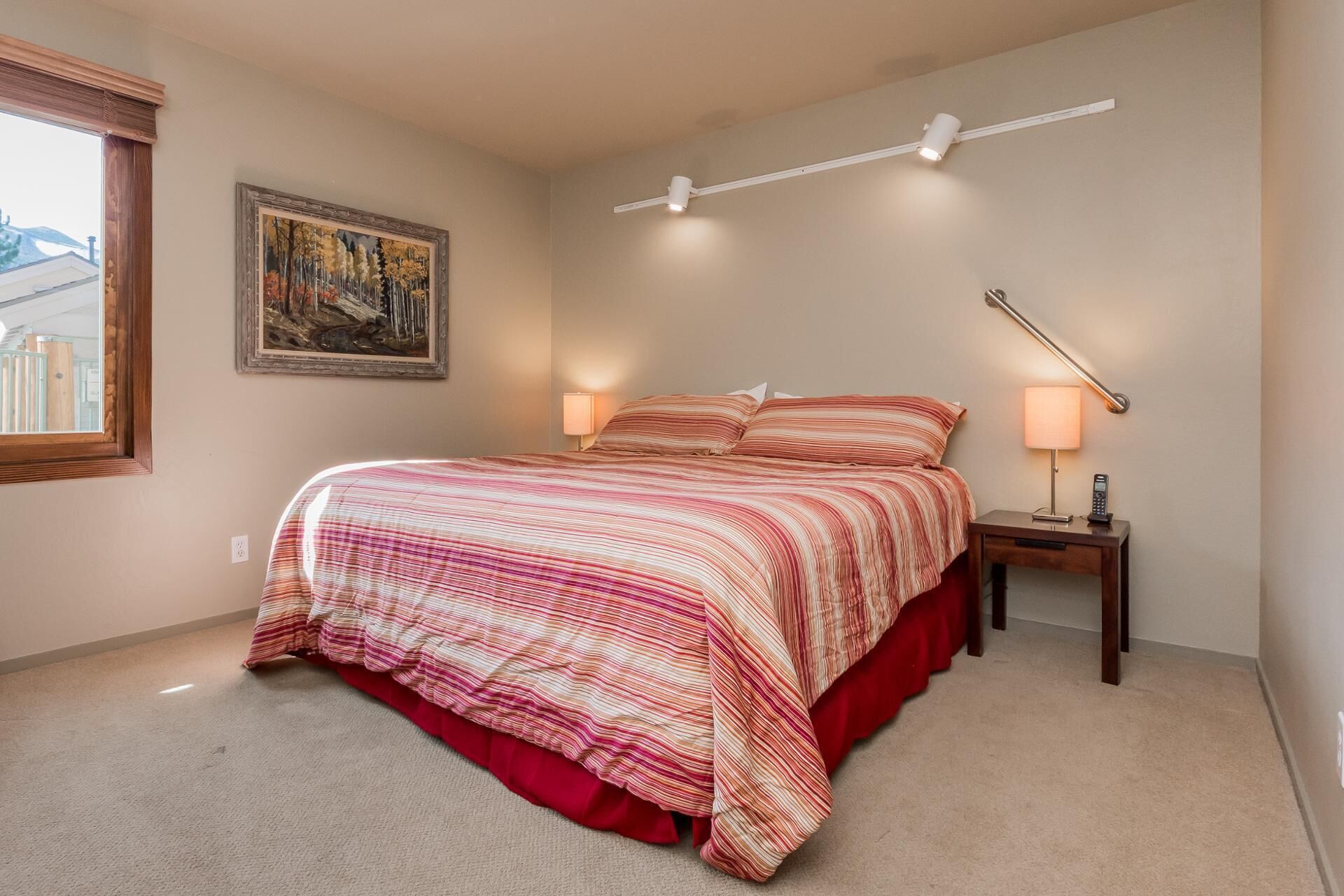 A bedroom with a bed, bedside lamps, a painting on the wall, and a window.