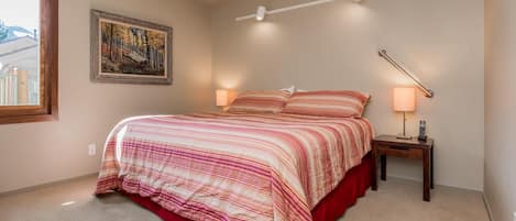 A bedroom with a bed, bedside lamps, a painting on the wall, and a window.