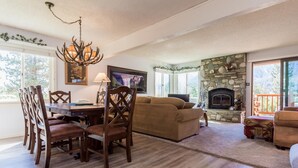 A living room with a stone fireplace, a dining area with a chandelier, and a sofa. - Mammoth Creek Unit 31 (Mammoth Lakes)