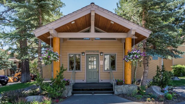 A lodge with a wooden facade, a green door, and a porch with hanging flower baskets. - Mammoth Creek Unit 31 (Mammoth Lakes)