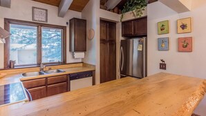 Une cuisine avec des meubles en bois, un réfrigérateur en acier inoxydable, un plan de travail en bois et une fenêtre donnant sur des arbres.