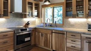 A modern kitchen with wooden cabinets, a stainless steel stove, and a window with a view of trees. - Mammoth Creek Unit 12 (Mammoth Lakes)