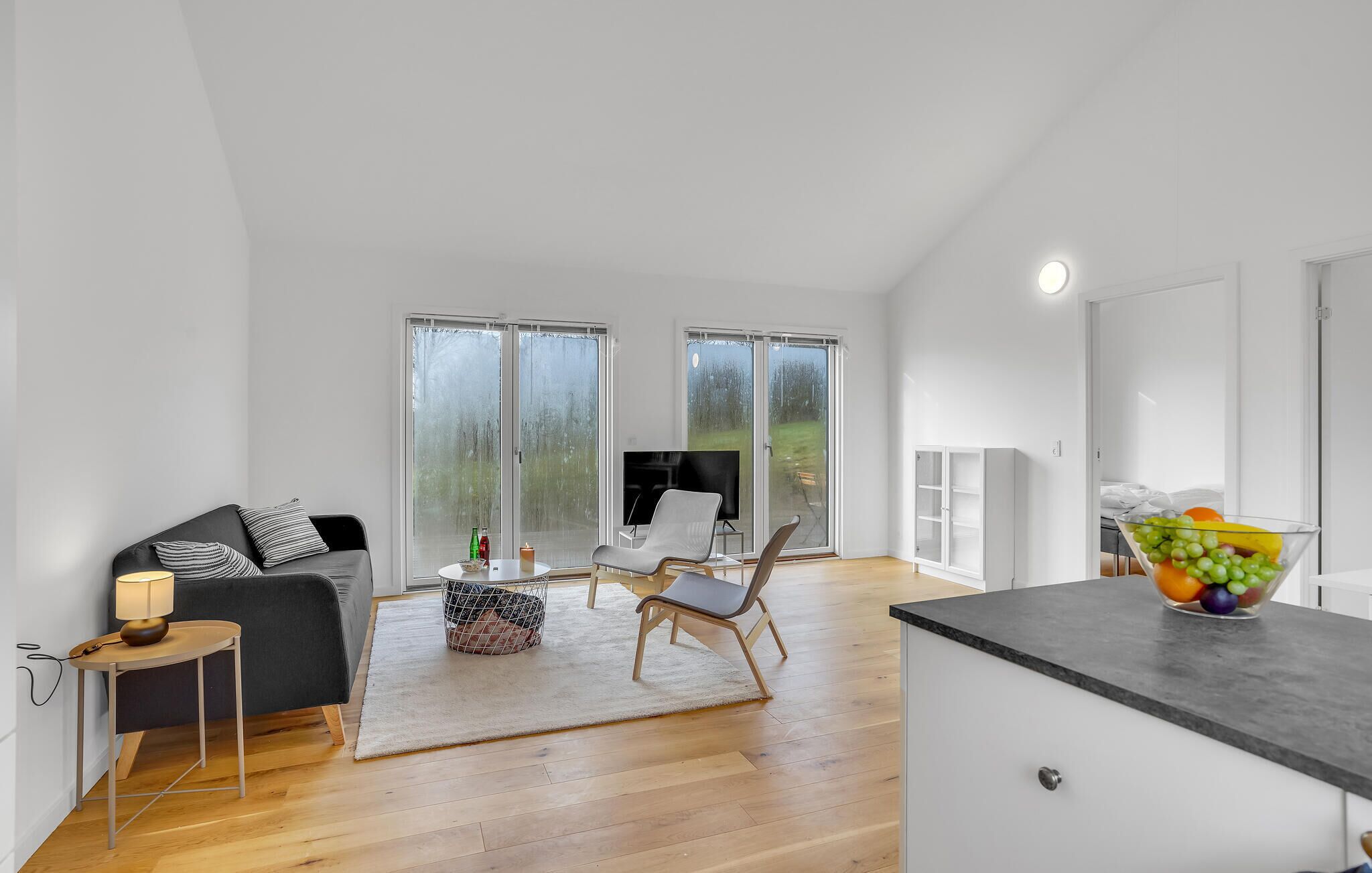 A spacious living area with a sofa, chairs, a TV, and a fruit bowl.