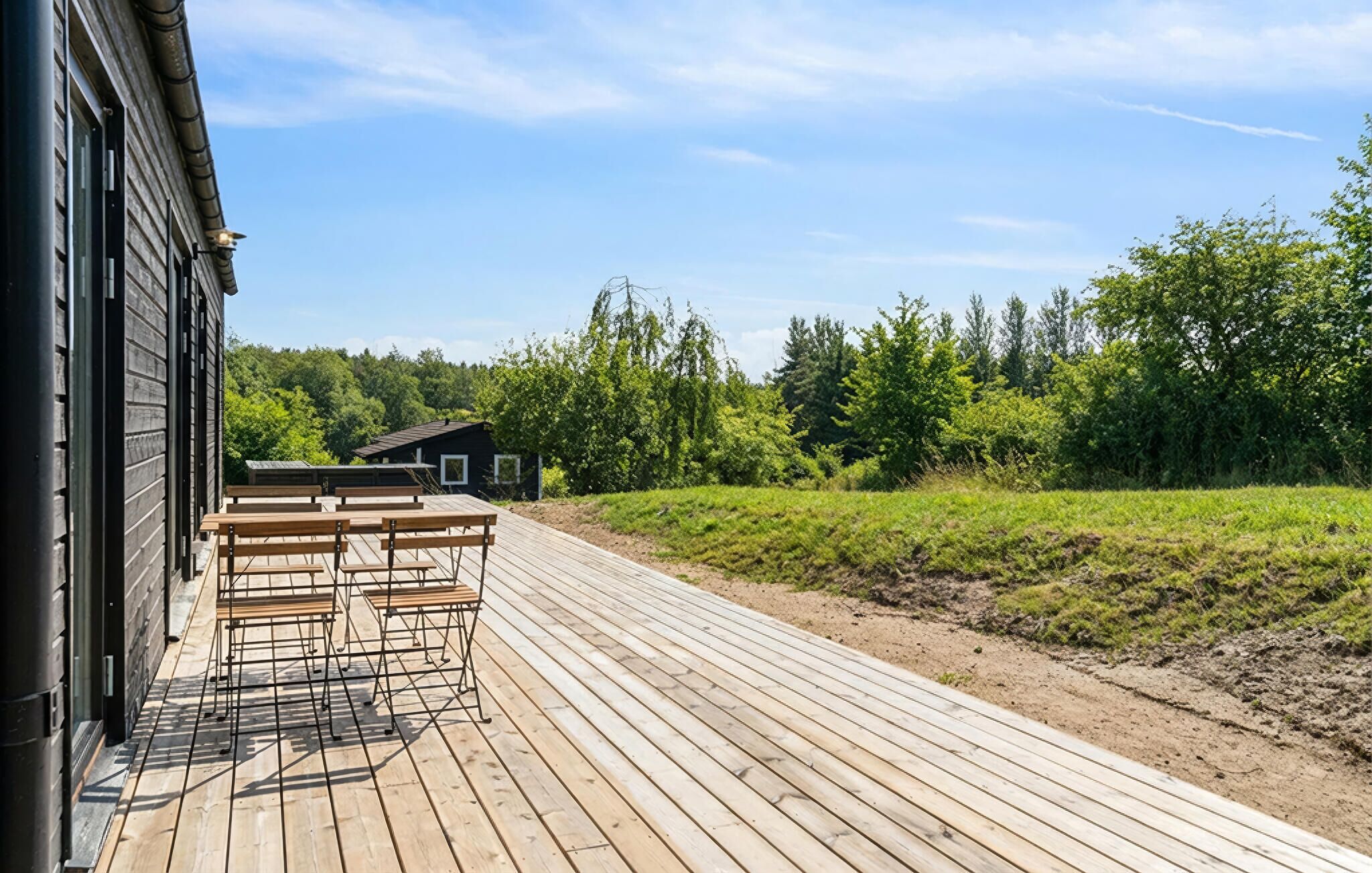 Une terrasse en bois avec des bancs, un bâtiment à la façade sombre et un paysage boisé en arrière-plan.