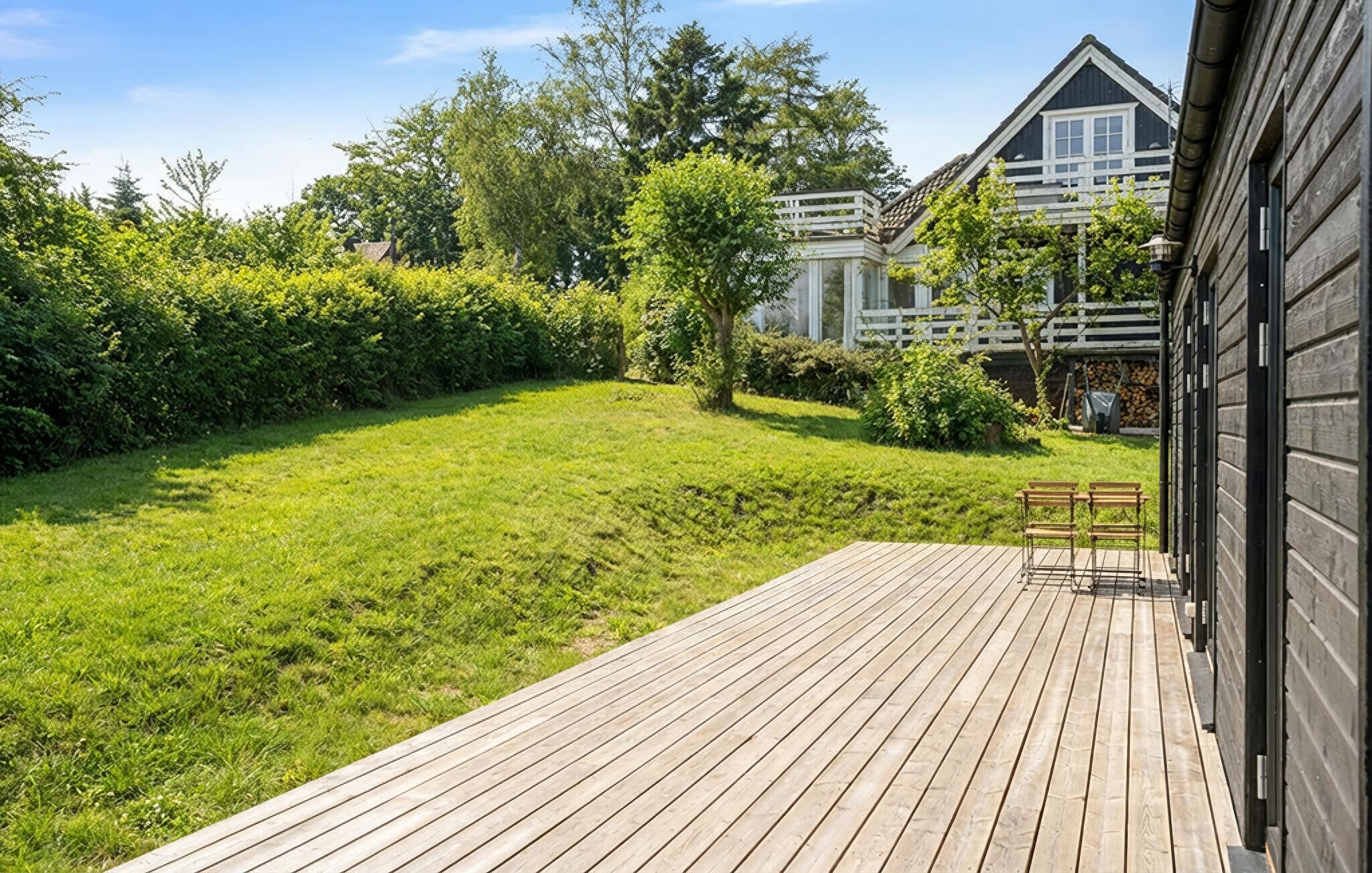 A wooden deck with a grassy lawn, a white fence, and a house with a dark roof and white trim.