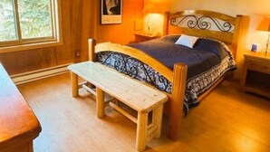 A cozy bedroom with a wooden bed, a bench, and a window with a view of trees. - Mammoth Creek Unit 32 (Mammoth Lakes)