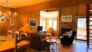 A spacious living room with a fireplace, wooden walls, and a dining area with chairs and a table. - Mammoth Creek Unit 32 (Mammoth Lakes)