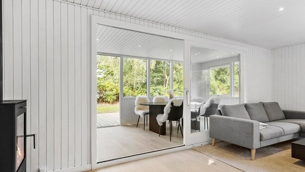 A modern living room with a grey sofa, a dining table with chairs, and a sliding glass door leading to an outdoor area. - Nice home in Farsø with house a panoramic view (Farsø)