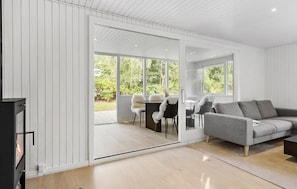 A modern living room with a grey sofa, a dining table with chairs, and a sliding glass door leading to an outdoor area.