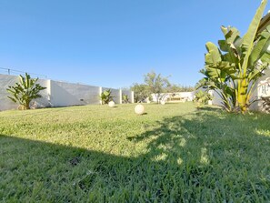 A well-maintained grassy area with large white spherical sculptures, a banana plant, and a white building in the background. - La Torre by Interhome (Ugento)