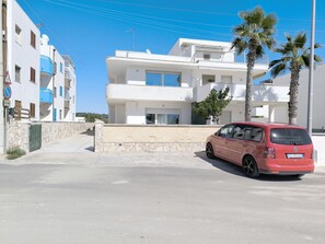 Um edifício moderno de dois andares com fachada de pedra, um carro vermelho estacionado em frente e palmeiras por perto.