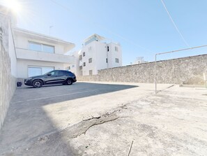 Ein Parkplatz mit einem schwarzen Auto, einem weißen Gebäude mit Balkonen und einer Steinmauer.