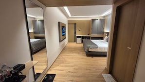 Et moderne hotelværelse med trægulv, seng, skrivebord og garderobeskab.