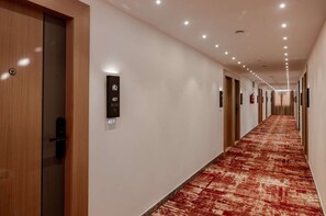 A hotel corridor with a red carpet, wooden doors, and numbered signs indicating room locations. - R D Hotels Bellandur (bangalore)