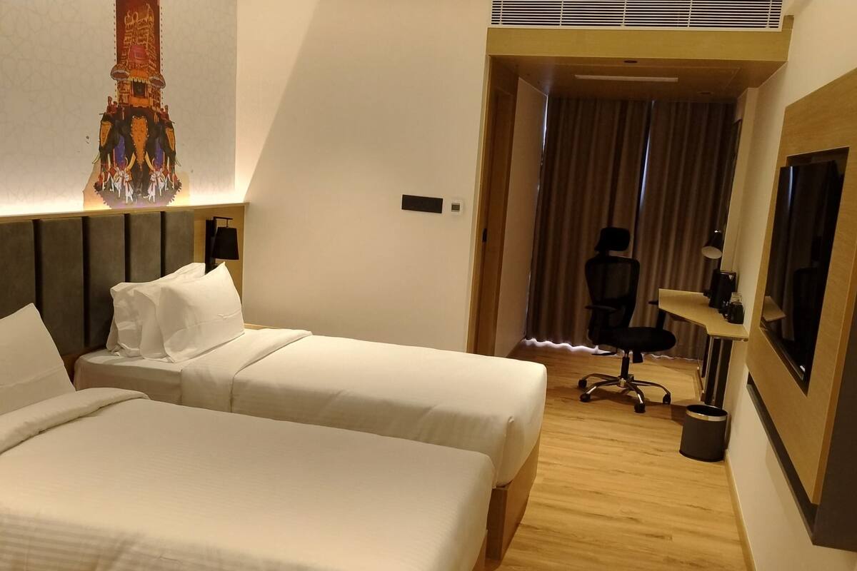 Habitación de hotel con dos camas, un escritorio, una silla y un espejo grande.