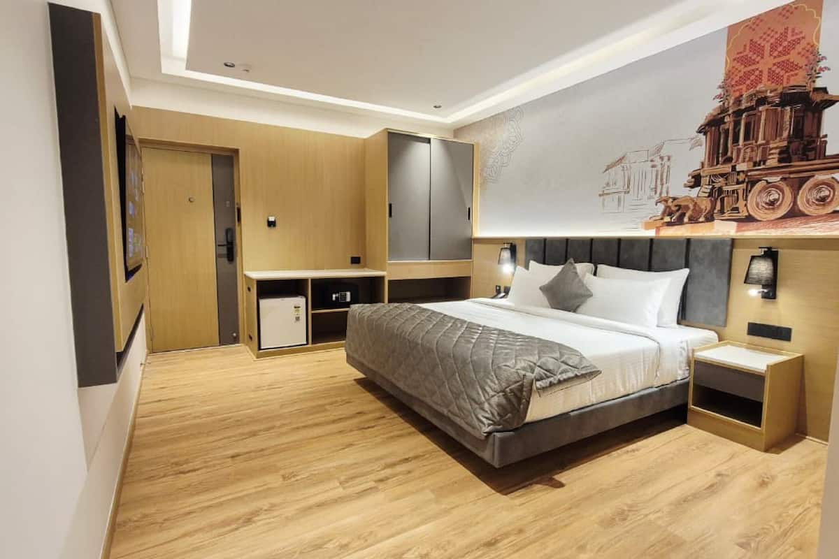 Una habitación de hotel moderna con una cama grande, un armario, un escritorio y un televisor montado en la pared.