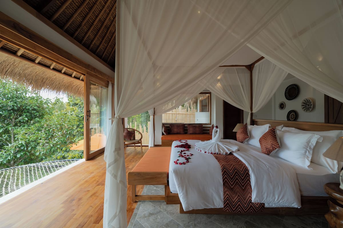 A bedroom with a bed, a bench, and a view of greenery.