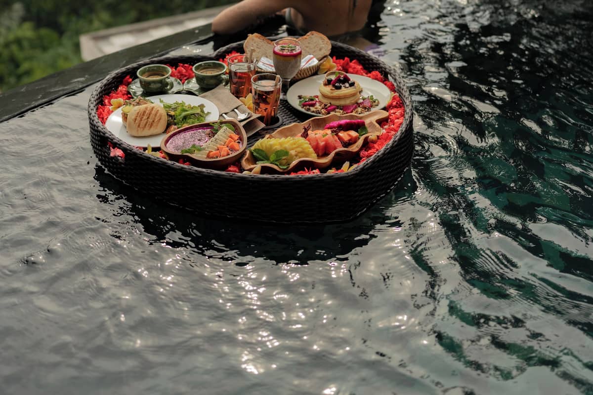 A person relaxing in a pool with a floating dining setup.