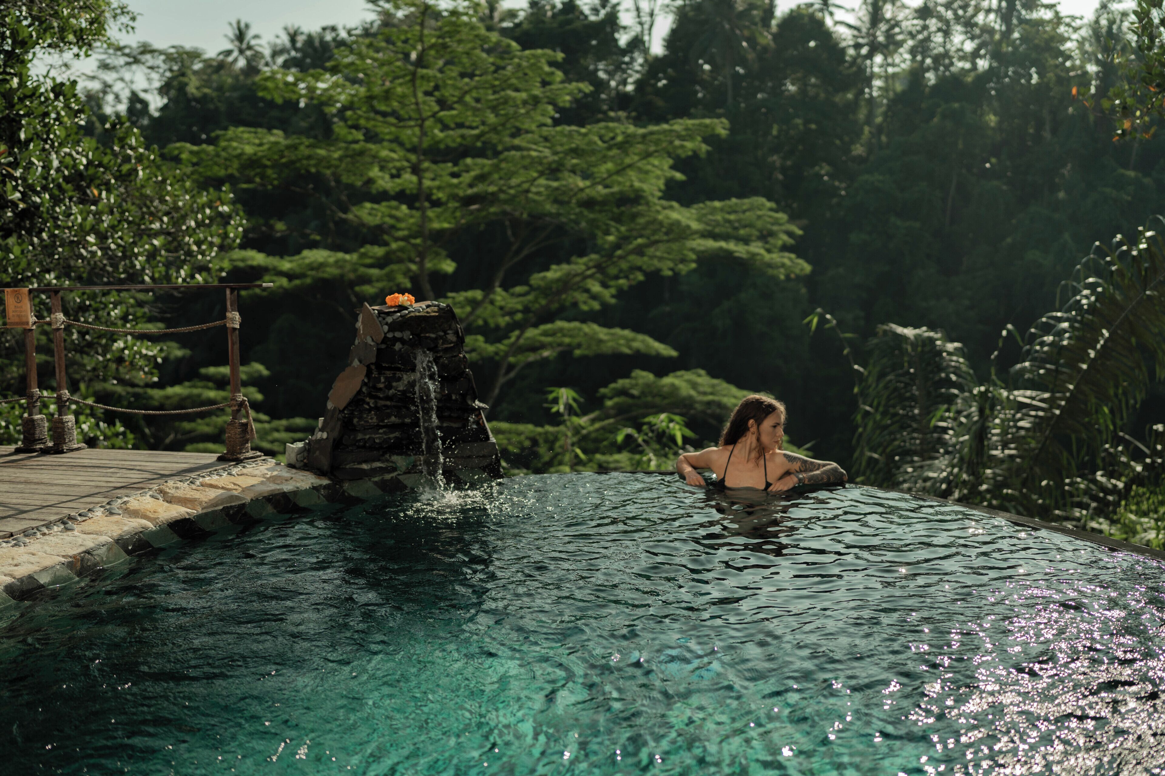 A pool with clear water, a waterfall feature, and lush greenery in the background.