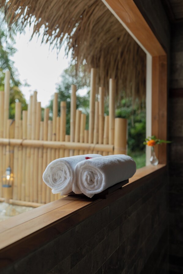 A wooden bench with rolled white towels placed on it, a bamboo fence, and a window with a view of greenery. - Marangga ubud valley view & private pool (Ubud)