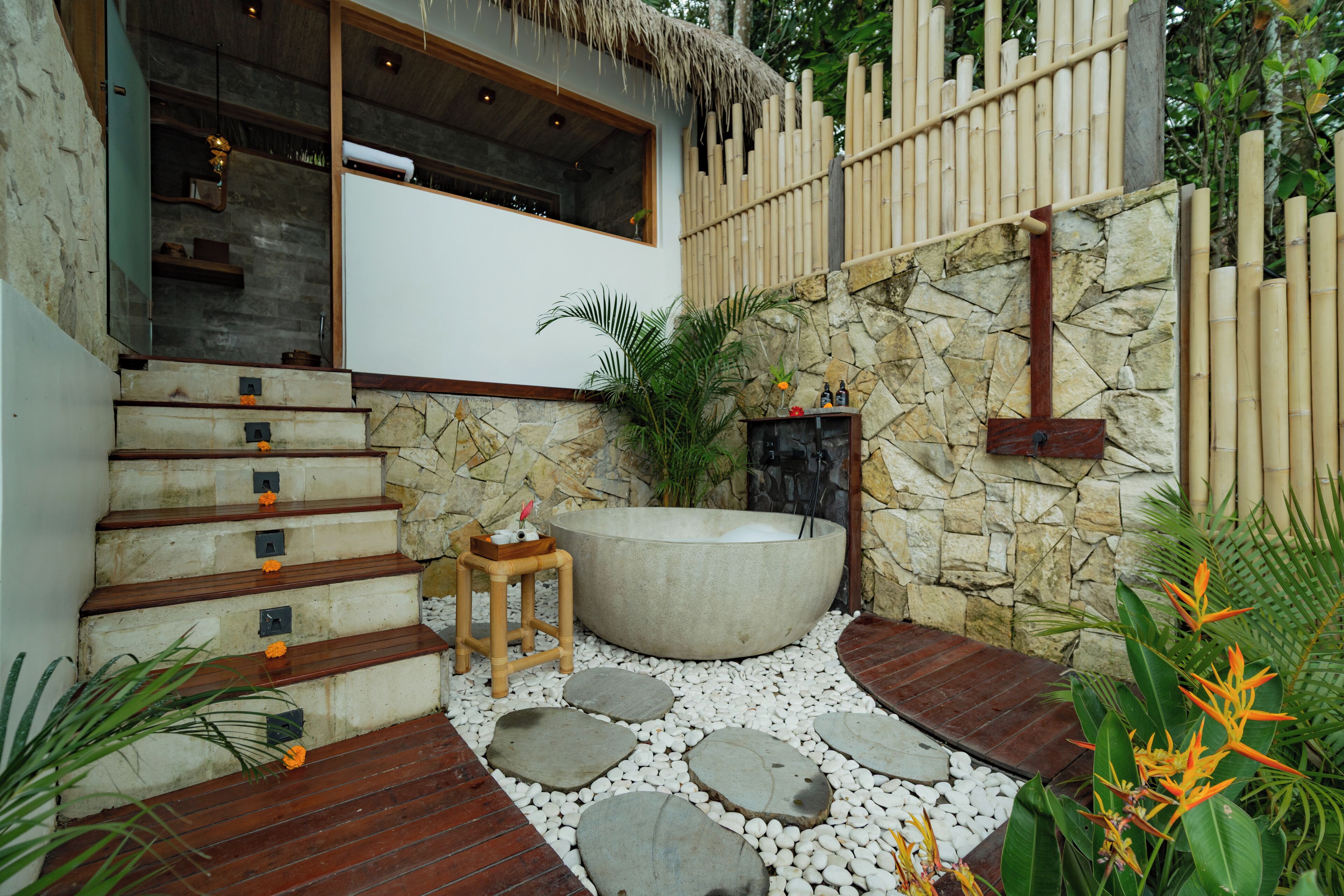 Un baño con paredes de piedra, una bañera grande, escalones de madera y un taburete pequeño.