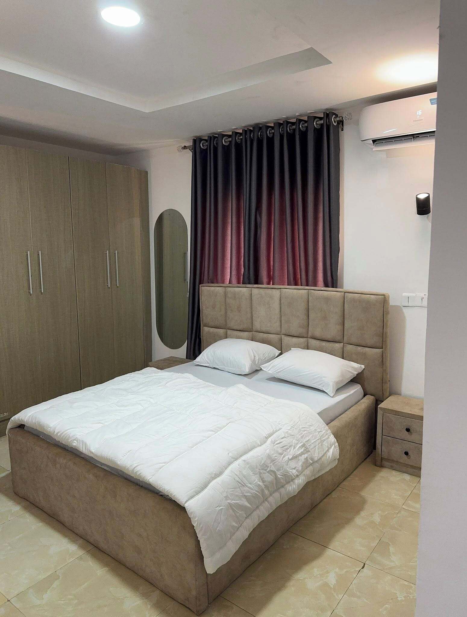 Un dormitorio con cama, armario, mesita de noche y aire acondicionado.