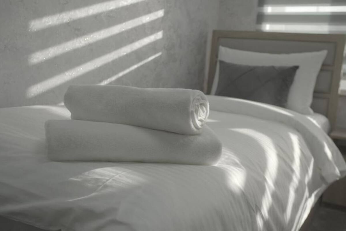 A neatly made bed with a rolled white towel, a pillow, and a wooden headboard.