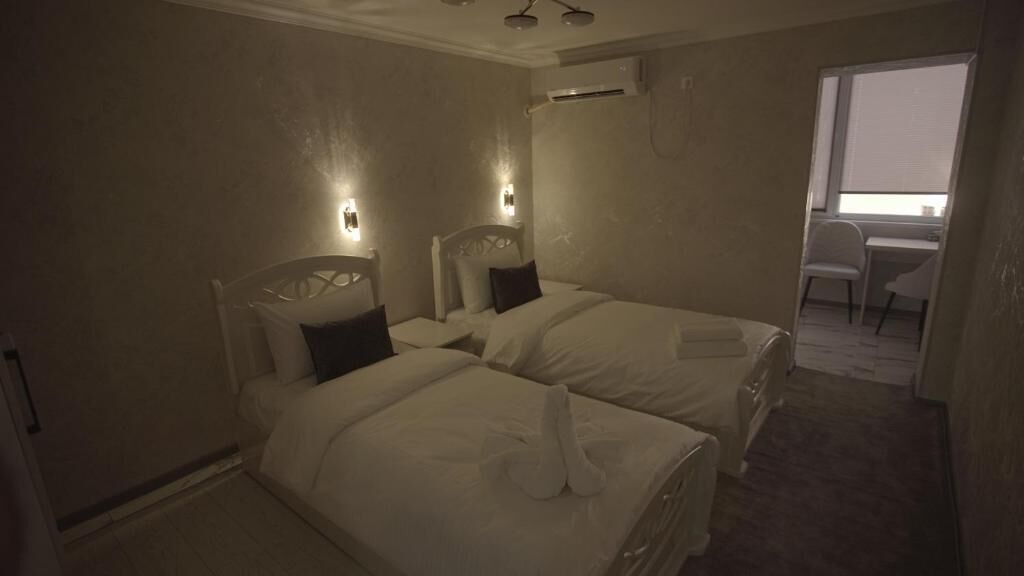 A hotel room with two beds, each with a headboard and pillows, a small desk, and a chair.