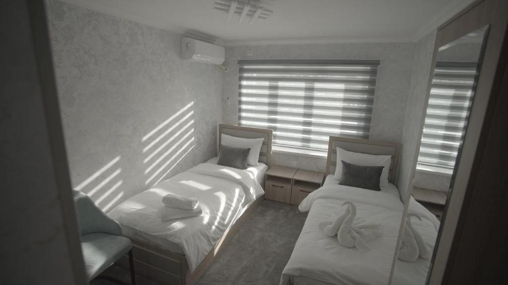 Ein kleines Hotelzimmer mit zwei Einzelbetten, einem kleinen Schreibtisch und einem Stuhl.