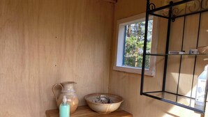 A wooden shelf with a ceramic pitcher and bowl, a window with a view of trees, and a metal rack with bottles. - Off Grid at Fjätälven (Sarna)