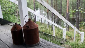 Two metal lanterns on a wooden deck with a white railing, overlooking a forested area. - Off Grid at Fjätälven (Sarna)